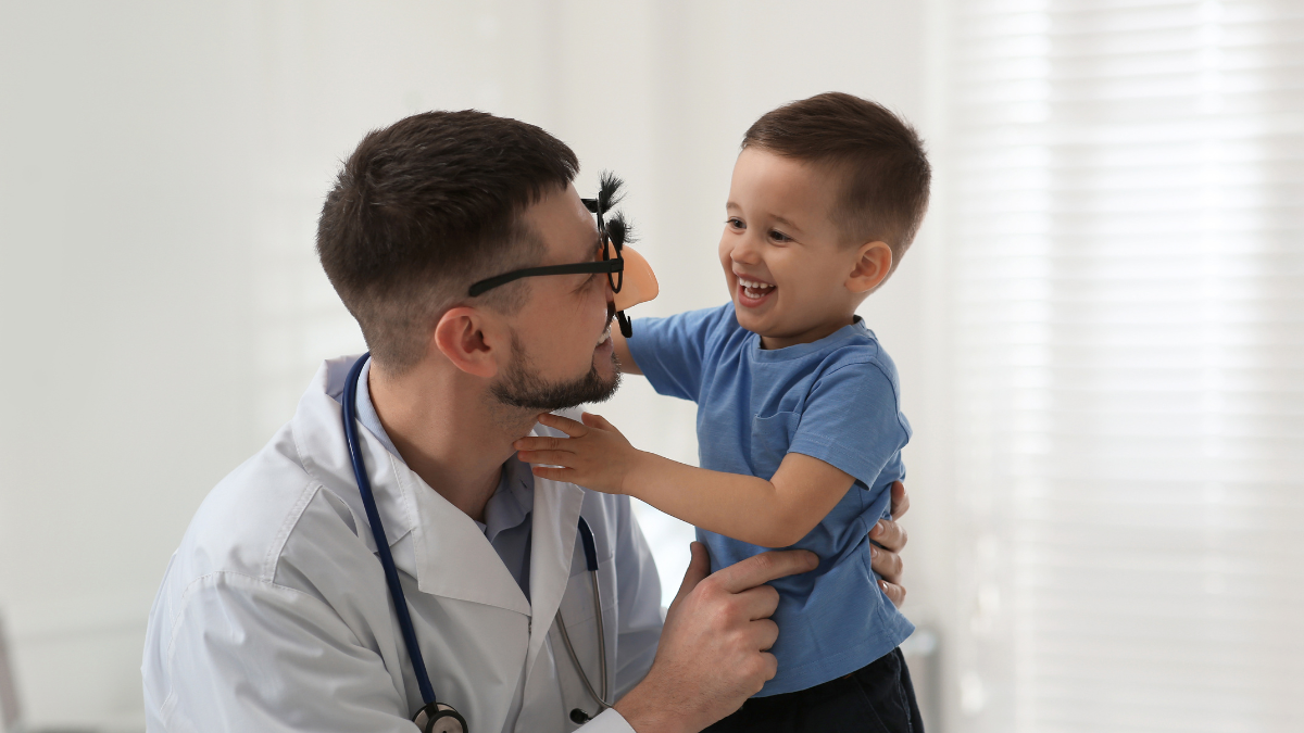 What Is Direct Primary Care? How It Works, What It Costs and Who It's For 4 Smiling young boy playing with a doctor wearing funny glasses during a visit